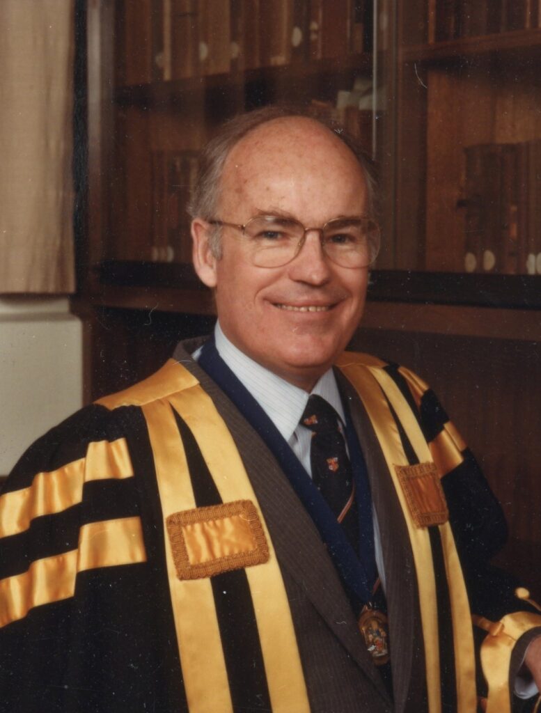 A man wearing an academic gown in black with gold stripes, indicating his position as dean of a medical faculty.